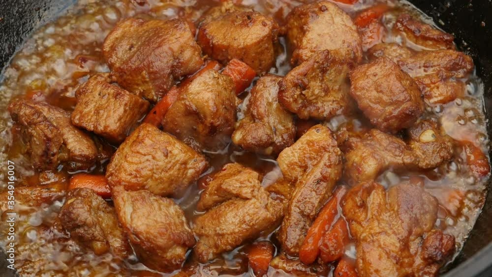 Cooking process, frying pork meat with carrots and onion in large cauldron on open fire. Close up. Cooking process, frying pork meat with carrots and onion in large cauldron on open fire. Close up.