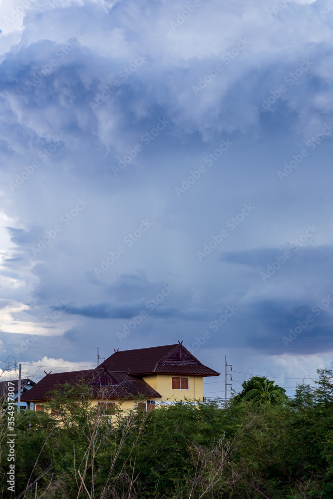 Cloudy sky above a home near the bush.