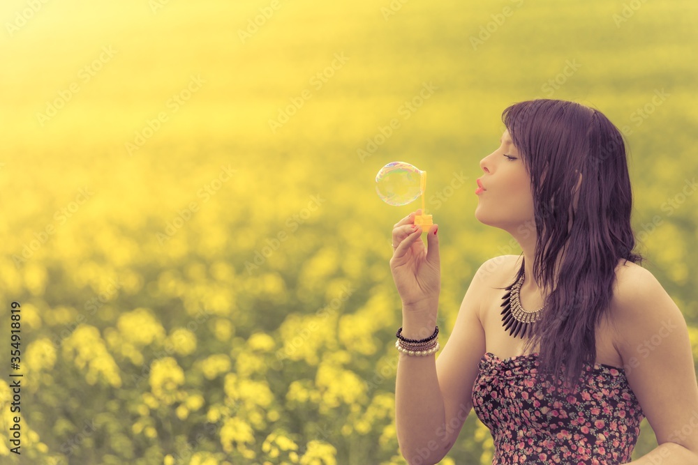 Beautiful woman blowing a single soap bubble in summer nature. The girl has fun in a yellow meadow and is enjoying her youth Beautiful woman blowing a single soap bubble in summer nature. The girl has fun in a yellow meadow and is enjoying her youth
