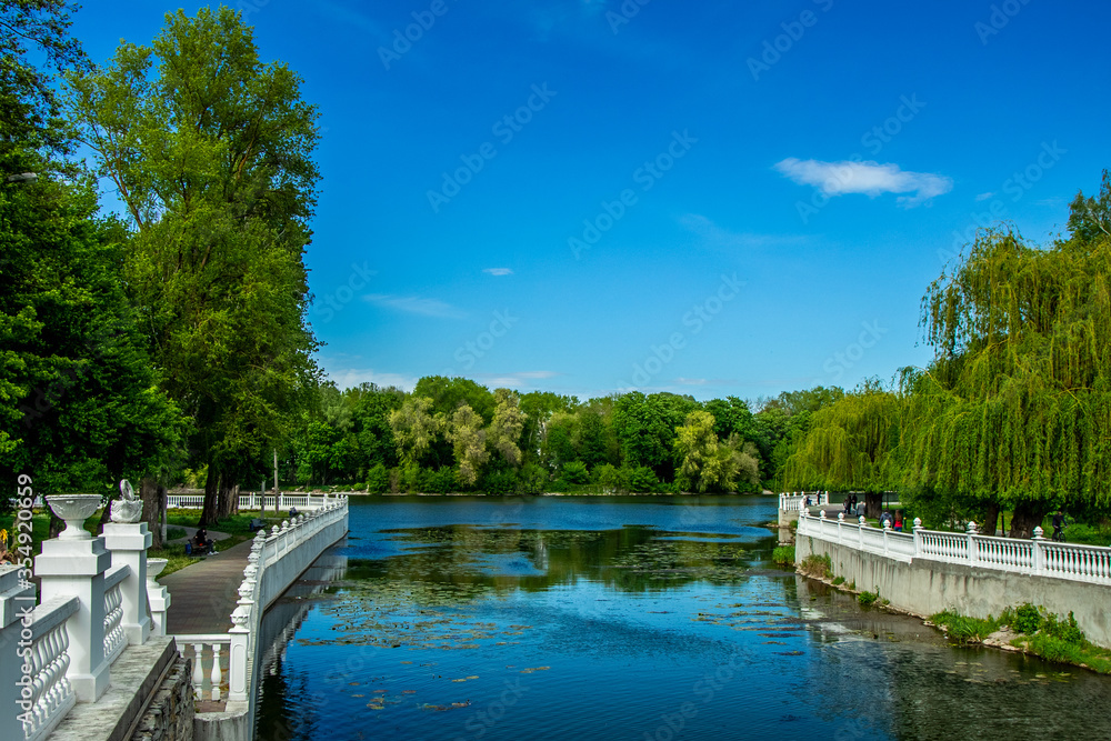 summer day time park landscape walking district area waterfront fence by marble palisade along river stream, green trees foliage and blue sky background scenic