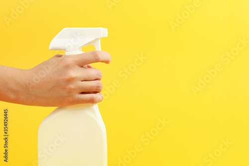 Woman hand holding spray with detergent on yellow background.