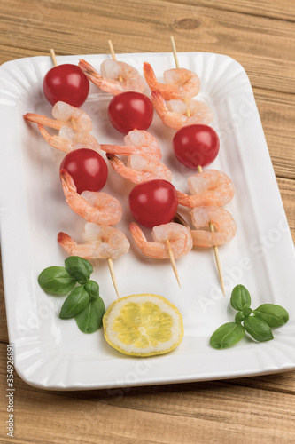 Shrimps with cucumber and tomatoes on skewer in white plate.