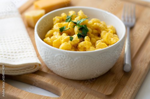Traditional American macaroni and cheese comfort food (also called mac n cheese) with elbow pasta coated in a cheesy creamy cheddar sauce. Topped with parsley, cheese in the background.
