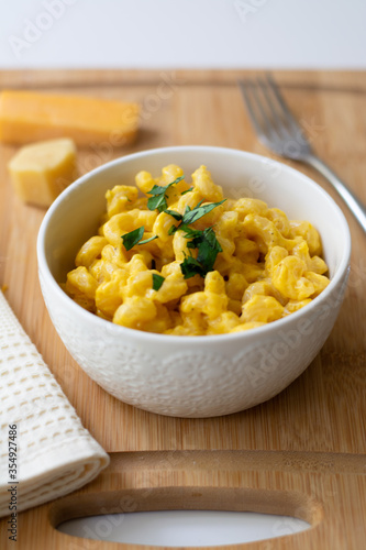 Traditional American macaroni and cheese comfort food (also called mac n cheese) with elbow pasta coated in a cheesy creamy cheddar sauce. Topped with parsley, cheese in the background.
