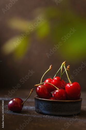 Fresh cherry in a bowl on black background. Fresh ripe sweet cherries with natural day light. Dark key photography, selective focus, copy space. Summer berries concept. Sweet organic berries.