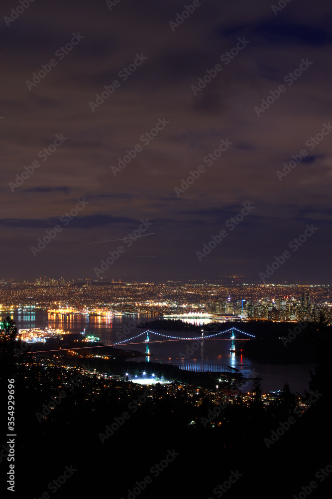 Lions Gate Bridge and Vancouver Night vertical. The Lions Gate Bridge at night with Stanley Park and downtown Vancouver in the background.

