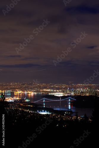 Lions Gate Bridge and Vancouver Night vertical. The Lions Gate Bridge at night with Stanley Park and downtown Vancouver in the background.