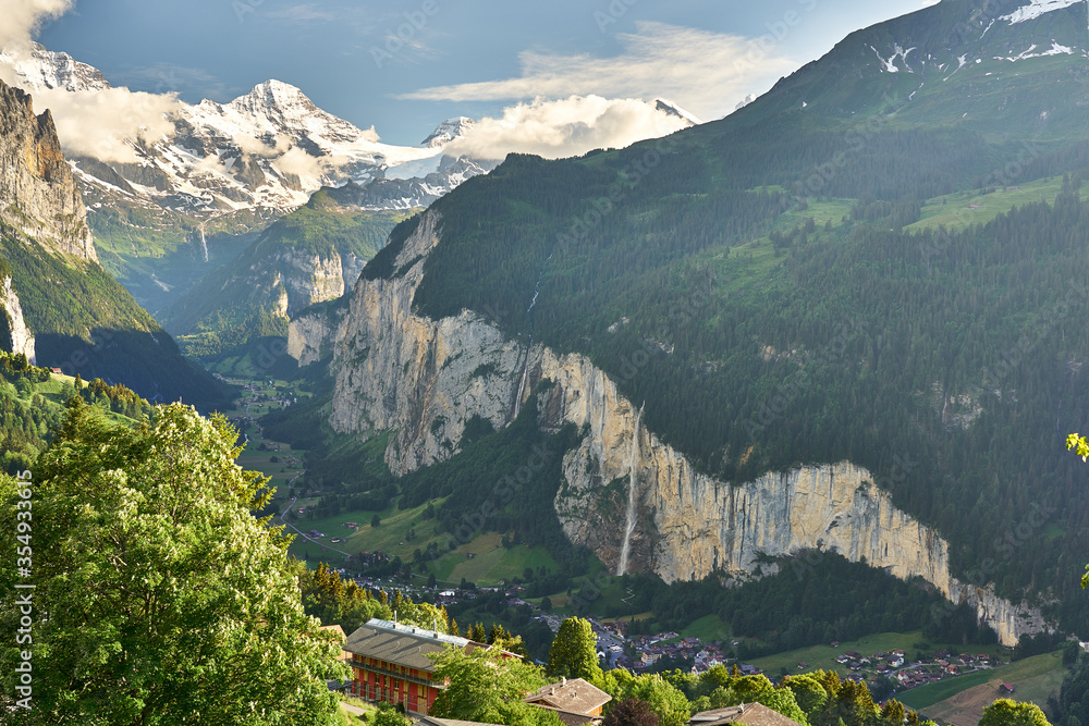 Fototapeta premium Lauterbrunnen Valley at sunset with snowy mountains, waterfall and green nature. Landscape panorama taken from mountain village Wengen, Switzerland