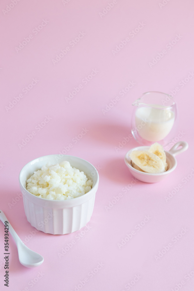 Rice milk porridge with banana slices, daughter and milk on a pink background, top view, flat lay. Rice milk porridge with banana slices, daughter and milk on a pink background, top view, flat lay.