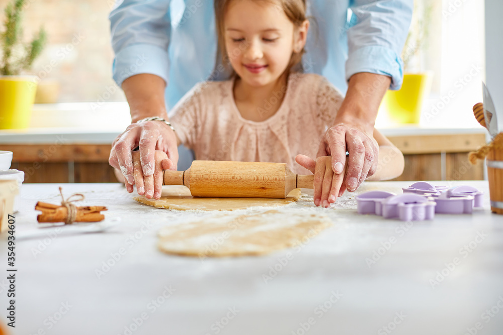 Father showing his little daughter how to roll dough for cookies Father showing his little daughter how to roll dough for cookies