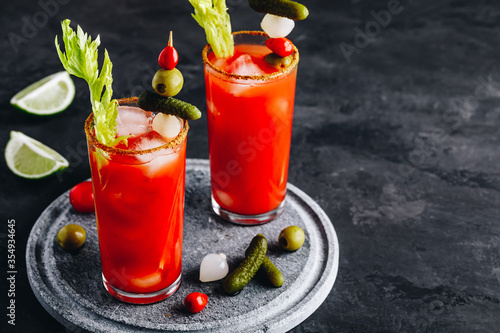Bloody Mary Cocktail in glasses with garnishes. Tomato Bloody Mary ice cold drink with fresh celery, pickles and lime