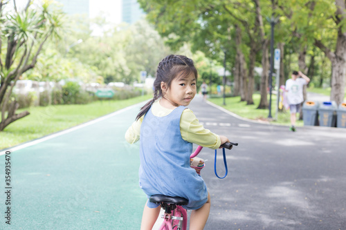 Portrait of little asian girl on a bicycle in summer city park outdoors