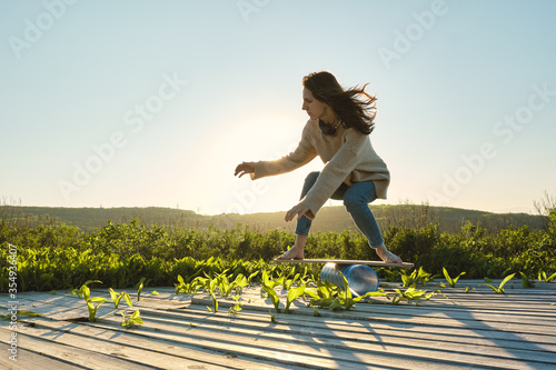 side view of healthy beautiful active woman keeping balance on the wooden balance board against the sky background at sunset summer day. Training and outdoor concept.