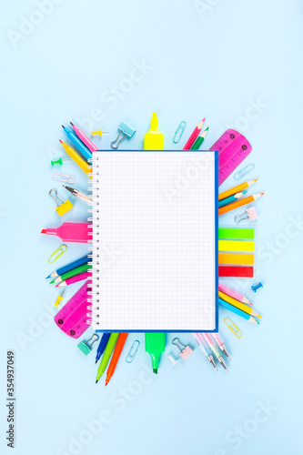 Checked notebook surrounded by various school office and painting supplies on blue background. Back to school concept. Top view. Copy space