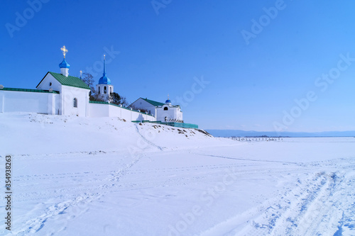 Russian Orthodox Church in russian Buryatia. Complex of Posolsky monastery buildings, Christian crosses in a small cemetery and the remains of a pier on the winter shore of lake Baikal