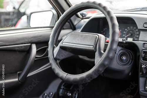 A close-up of the steering wheel of a Russian old car on a black plastic control panel with an ignition switch and sensors for engine speed and temperature inside the passenger compartment. © Aleksandr Kondratov
