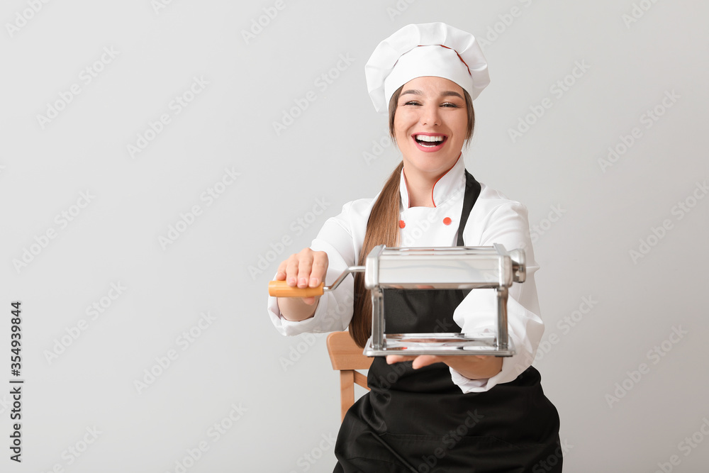 Young female chef with pasta machine on light background Young female chef with pasta machine on light background