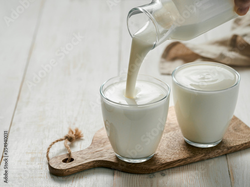 Pouring homemade kefir, buttermilk or yogurt with probiotics. Yogurt flowing from glass bottle on white wooden background. Probiotic cold fermented dairy drink. Trendy food and drink. Copy space left photo