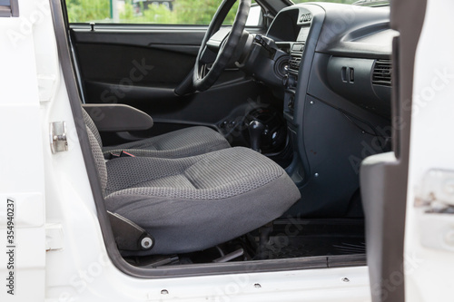 An open front passenger door of an old white Russian car with seats covered in gray cloth and with a black plastic control panel, a clean interior after dry cleaning is ready for sale.