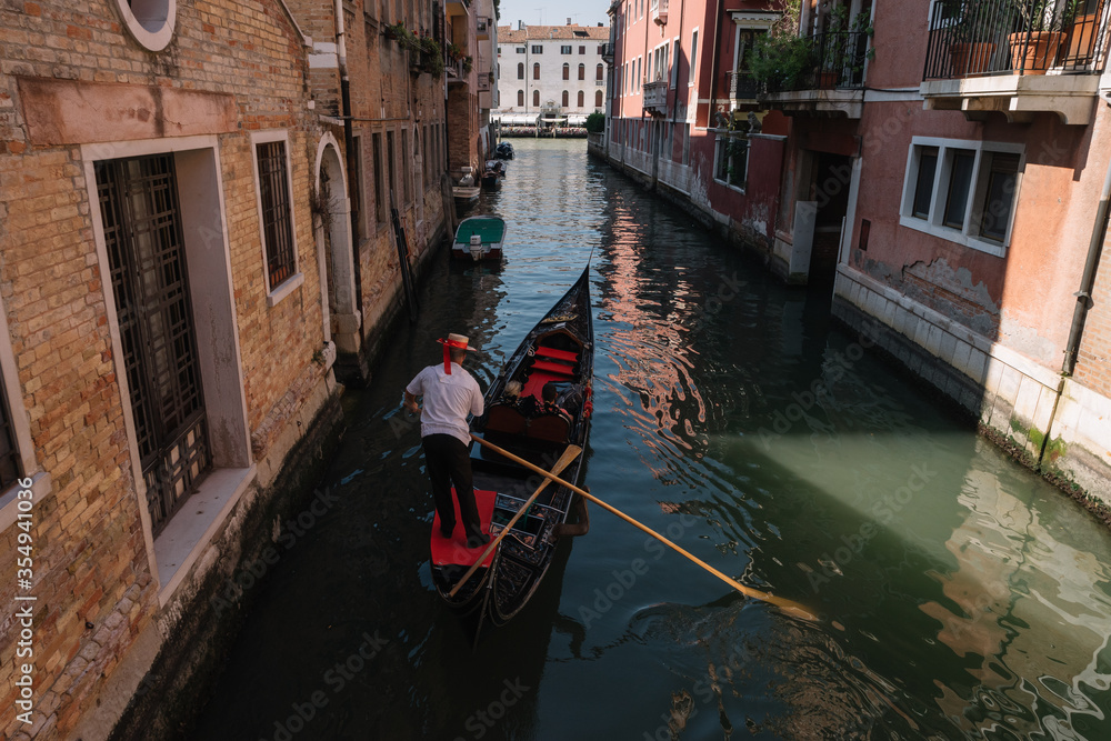 Gondolier drives a gondola with two tourists on a canal in Venice, Italy.