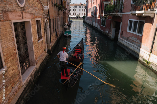 Gondolier drives a gondola with two tourists on a canal in Venice, Italy.