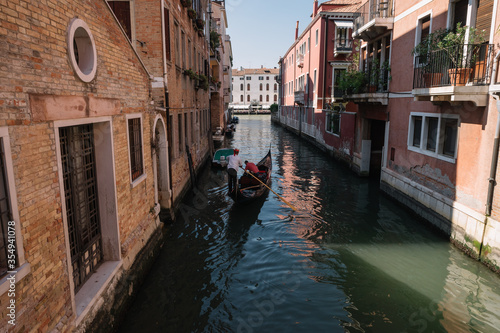 Gondolier drives a gondola with two tourists on a canal in Venice, Italy.