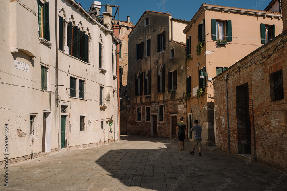 Tourists are walking along the narrow and bright streets of sunny Venice, Italy.