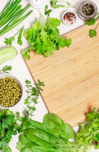 Cooking ingredients and a cutting board on a light background, top view, free space for text. Salad ingredients - spinach, lettuce, cucumbers, parsley flat lay. Food background. Diet and vegan food
