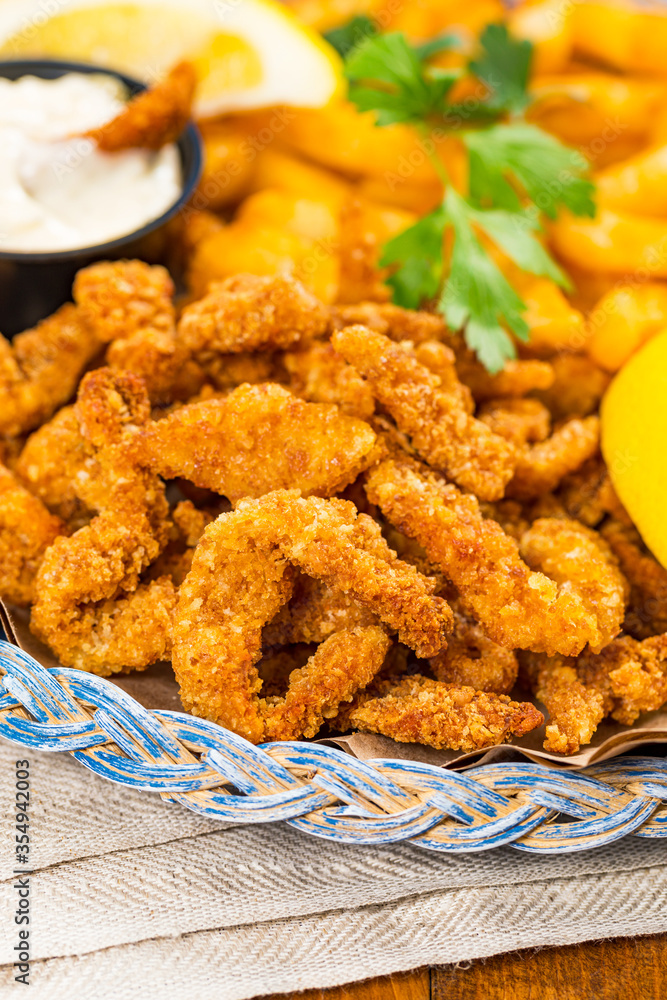 Crispy Breaded Clam Strips Snack Size. Deep Fried Breaded Clams Fingers and French Fried Potatoes with Tartar Dipping Sauce on a wooden board. Selective focus. Crispy Breaded Clam Strips Snack Size. Deep Fried Breaded Clams Fingers and French Fried Potatoes with Tartar Dipping Sauce on a wooden board. Selective focus.