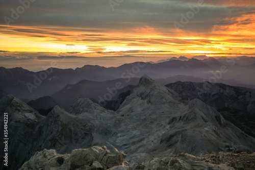 Early morning viewed from Triglav, the highest mountain in Slovenia just at dawn. Visible sun rising and shining above the valleys and mountain ranges in front