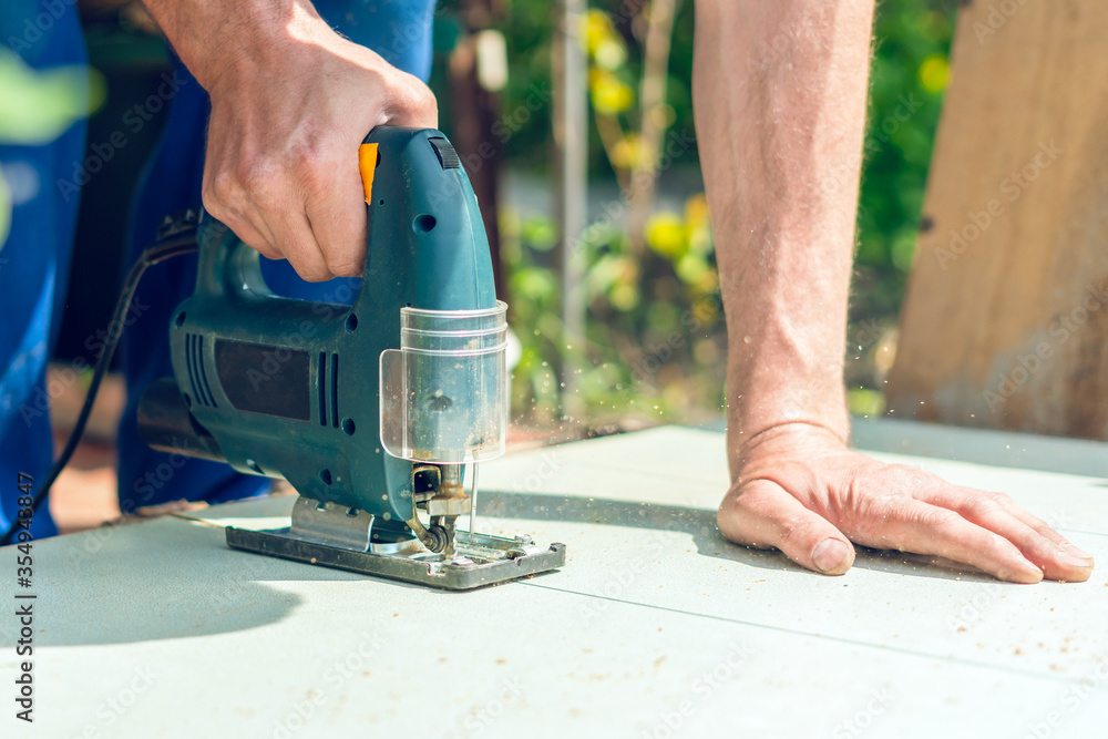 A carpenter saws a wooden cloth with an electric jig saw A carpenter saws a wooden cloth with an electric jig saw