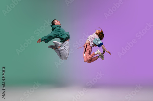 High jump. Boy and girl dancing hip-hop in stylish clothes on colorful gradient background at dance hall in neon. Youth culture, movement, style and fashion, action. Fashionable portrait. Street dance photo