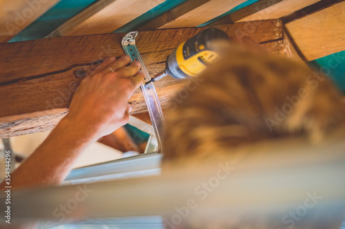 Картината върху платно Screwing tin holders for a drywall into a wood portion of a roof using a battery