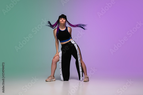 Fototapeta Naklejka Na Ścianę i Meble -  Beautiful sportive girl dancing hip-hop in stylish clothes on colorful gradient background at dance hall in neon light. Youth culture, movement, style and fashion, action. Fashionable bright portrait.