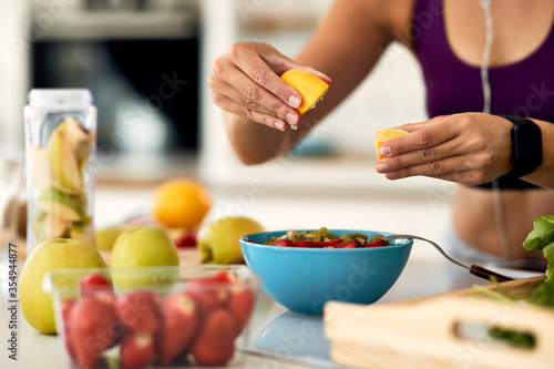 Close-up of woman squeezing lemon in fruit salad she is making in the kitchen.