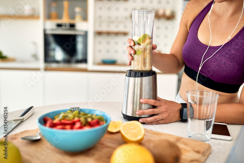 Unrecognizable athletic woman using blender and preparing smoothie in the kitchen.