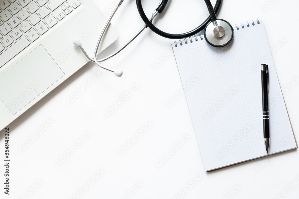 Workplace of doctor with laptop and stethoscope on keyboard and notepad with pen isolated. Top view. Concept medical, business. Backround Workplace of doctor with laptop and stethoscope on keyboard and notepad with pen isolated. Top view. Concept medical, business. Backround