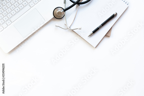Workplace of doctor with laptop and stethoscope on keyboard and notepad with pen isolated. Close up. Top view. Concept medical, business.