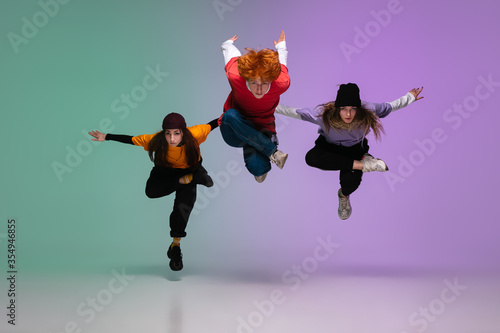 Group of teens, boys and girls dancing hip-hop in stylish clothes on colorful gradient studio background in neon light. Youth culture, movement, style and fashion, action. Fashionable portrait. photo