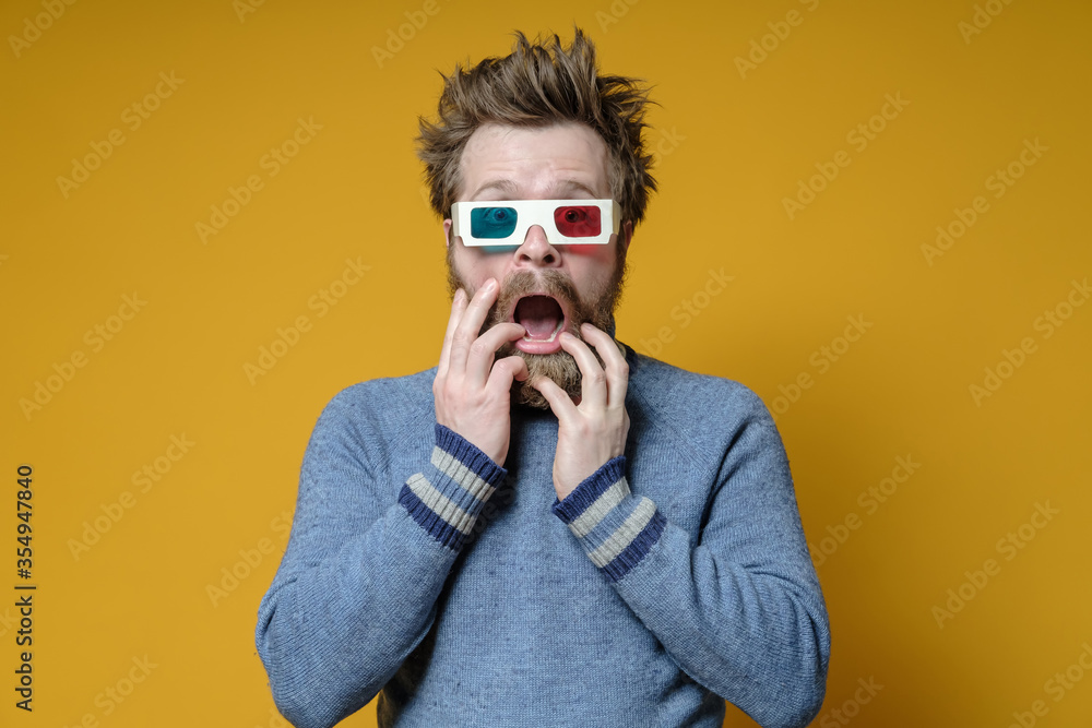 Portrait of a shaggy, bearded scared man in 3D glasses with an open mouth and big eyes, on a yellow background. Portrait of a shaggy, bearded scared man in 3D glasses with an open mouth and big eyes, on a yellow background.