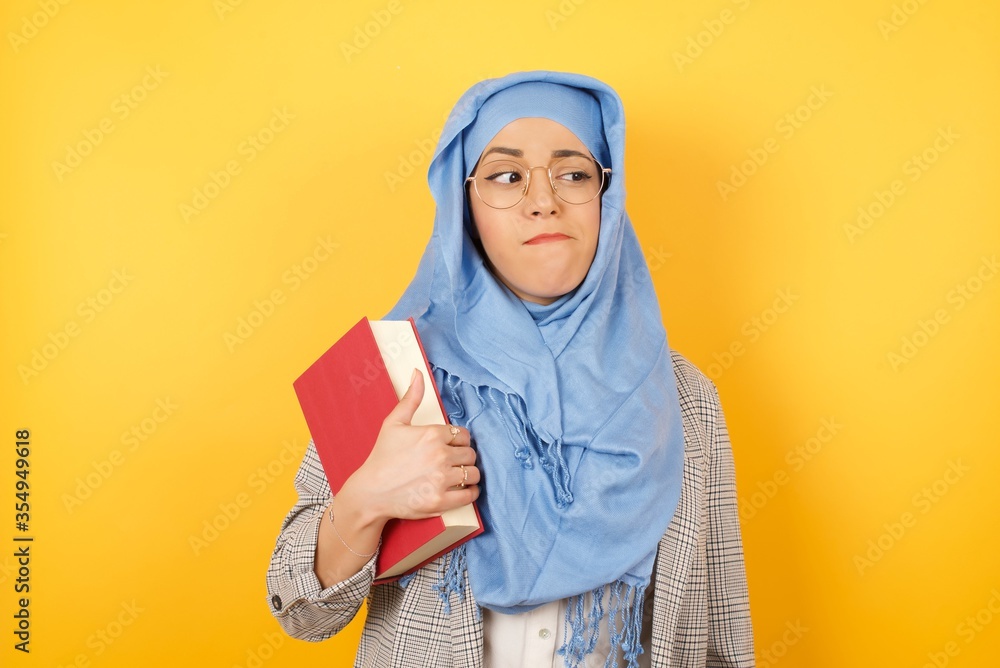 Photo of amazed puzzled young muslim woman wearing hijab female, curves lips and has worried look, sees something awful in front, isolated on studio background. Photo of amazed puzzled young muslim woman wearing hijab female, curves lips and has worried look, sees something awful in front, isolated on studio background.