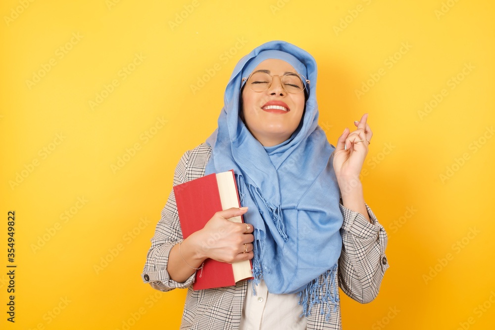I have to win. Joyful young muslim woman wearing hijab clenches teeth, raises fingers crossed, makes desirable wish, waits for good news, stands indoor over blank wall I have to win. Joyful young muslim woman wearing hijab clenches teeth, raises fingers crossed, makes desirable wish, waits for good news, stands indoor over blank wall