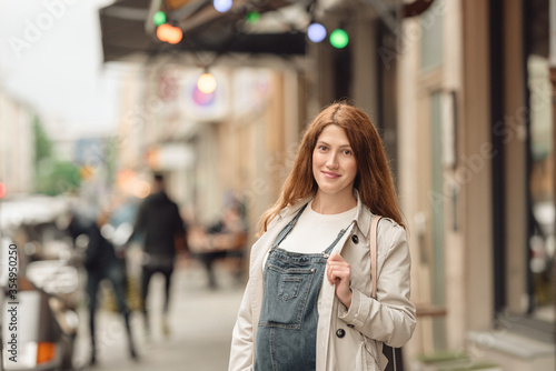 Beautiful young pregnant woman wearing casual clothes walking through the city streets. concept of motherhood and pregnancy. street portrait among cars close up view. © lialia699