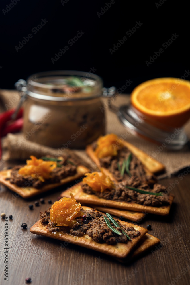A few crackers with poultry liver pate and orange jam, hot pepper and orange fruits on the sackcloth and wooden background