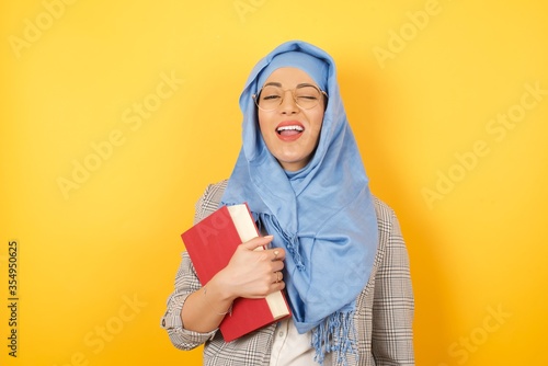 Cute young muslim woman wearing hijab blinking her eyes with pleasure having happy expression. Facial expressions and people emotions concept. © Jihan