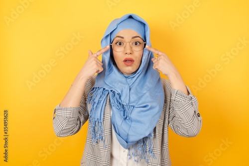 Playful excited tyoung muslim woman wearing hijab showing Ok gestures with both hands, pretending to wear spectacles, astonished to see something amazing. Emotions, body language and gesturesï¿½ photo