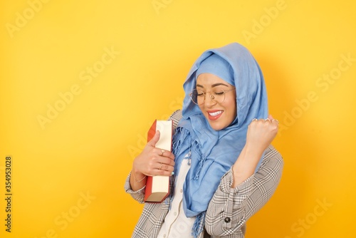 Young muslim woman wearing hijab rejoicing her success and victory clenching her fists with joy. Lucky Arab woman being happy to achieve her aim and goals. Positive emotions, feelings. © Jihan