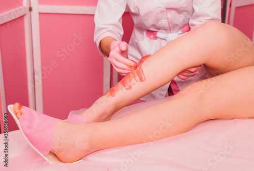 Sugaring. Young woman gets the procedure for hair removal liquid sugar. Beautician depilating young woman's legs with liquid sugar in spa center