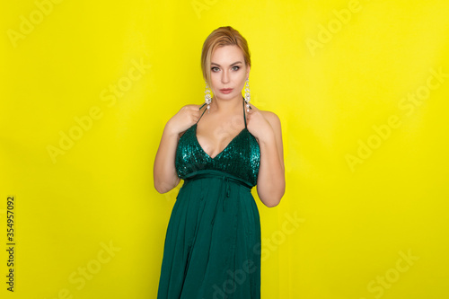 Blond woman wearing green evening dress over yellow background