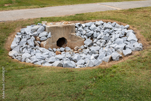 Aged cast concrete headwall for storm water runoff surrounded by new rocks, environmental safety, green grass copy space, horizontal aspect